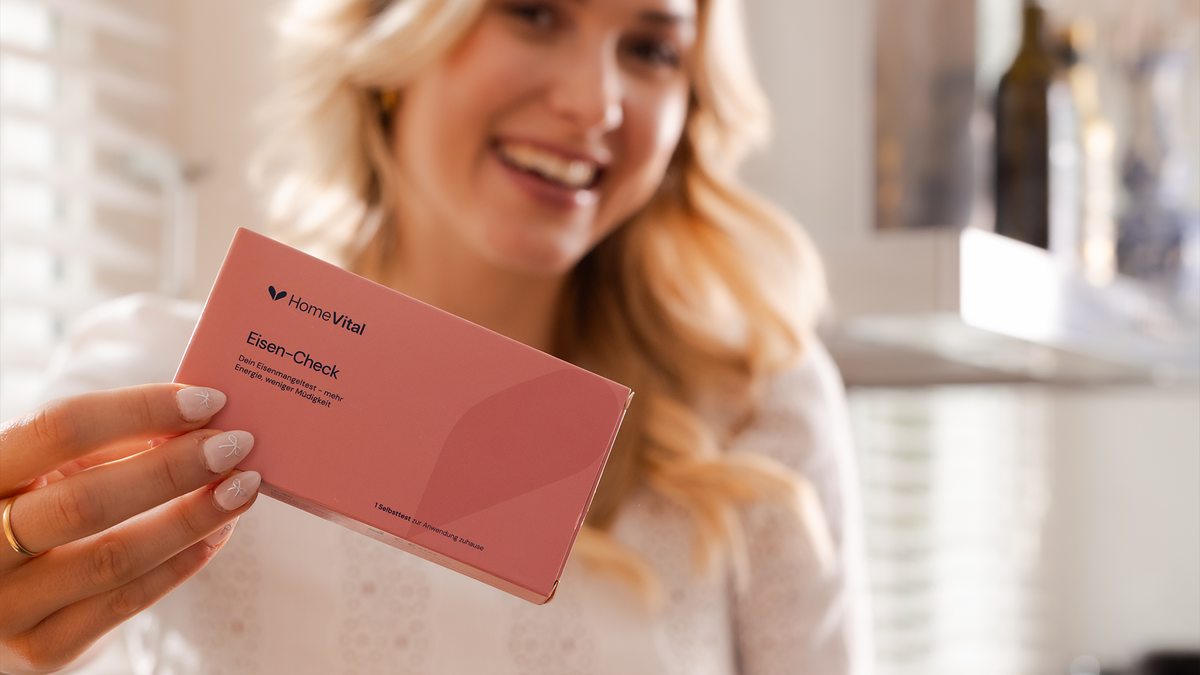 Lächelnde Frau hält den HomeVital Eisen-Check in der Hand