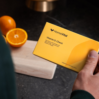 HomeVital Vitamin D-Check in der Hand, daneben eine halbe Orange